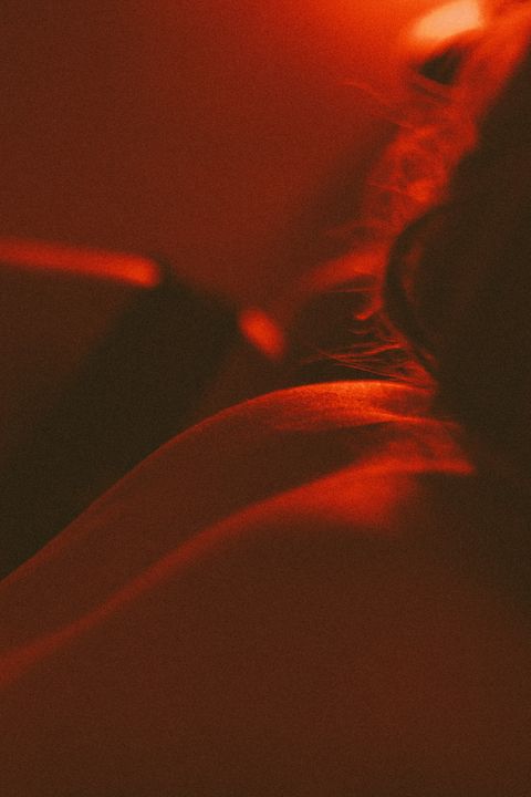 Deux personnes en harnais et lingerie, une main posée sur une jambe, dans la lumière rouge d'une soirée BDSM